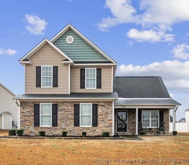 view of front of home with a front lawn, stone siding, and roof with shingles