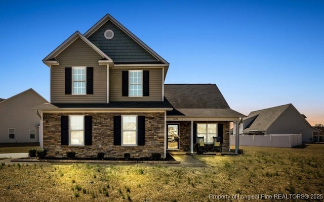 view of front of house with stone siding, a front lawn, and fence