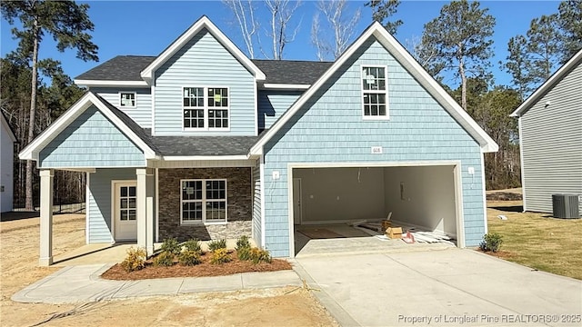 view of front of property featuring roof with shingles, concrete driveway, central AC unit, a garage, and stone siding