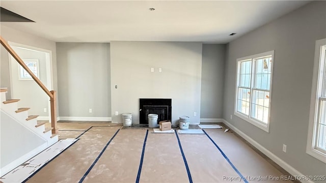 unfurnished living room with stairs, a fireplace with flush hearth, and baseboards