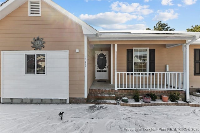 snow covered property entrance with a porch