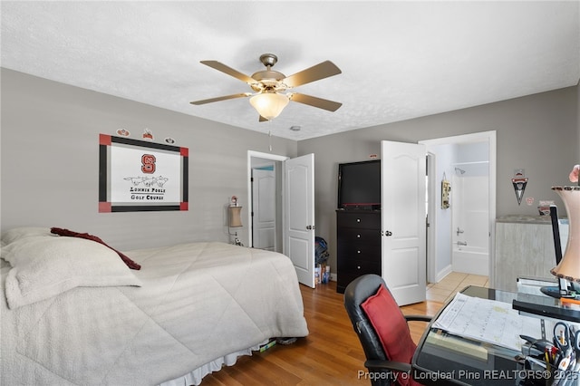 bedroom featuring light wood-type flooring, a textured ceiling, ceiling fan, and ensuite bath