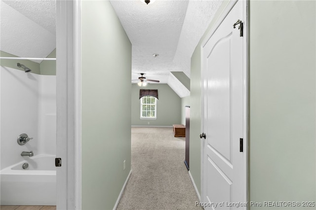 hall with light carpet, lofted ceiling, and a textured ceiling