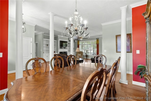 dining room featuring an inviting chandelier, built in shelves, ornamental molding, and decorative columns