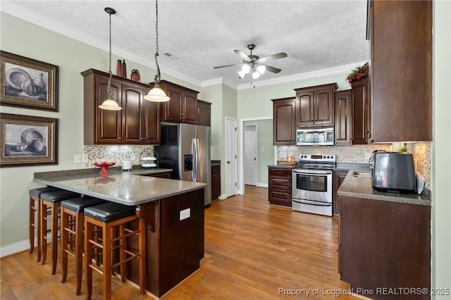 kitchen featuring a breakfast bar area, hanging light fixtures, a textured ceiling, appliances with stainless steel finishes, and kitchen peninsula