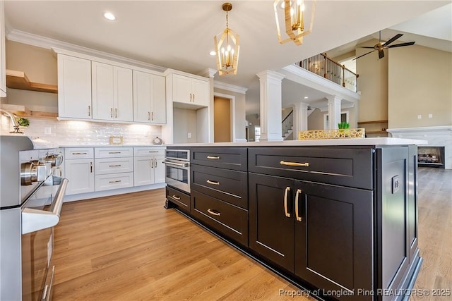 kitchen featuring white cabinetry, stainless steel oven, crown molding, and decorative light fixtures