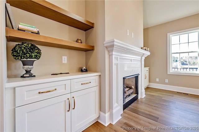 bar featuring white cabinetry, a fireplace, and light wood-type flooring