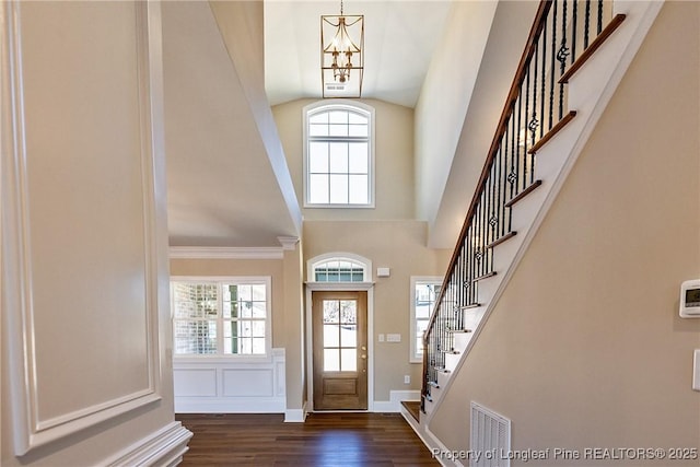 entrance foyer with dark wood-type flooring, a wealth of natural light, high vaulted ceiling, and a chandelier