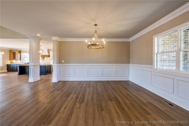 unfurnished dining area with decorative columns, crown molding, dark wood-type flooring, and a chandelier