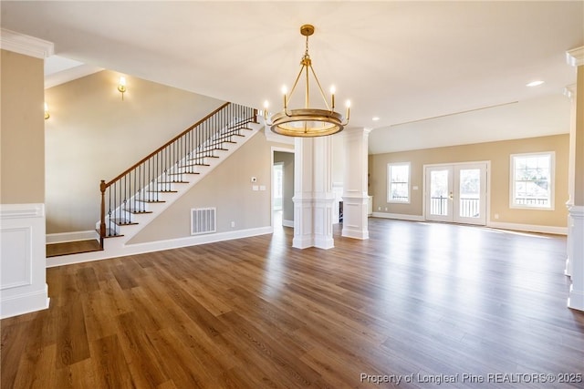 unfurnished living room featuring dark hardwood / wood-style flooring, decorative columns, french doors, and a chandelier