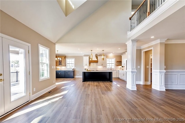 unfurnished living room featuring hardwood / wood-style floors, a towering ceiling, ornamental molding, and ornate columns