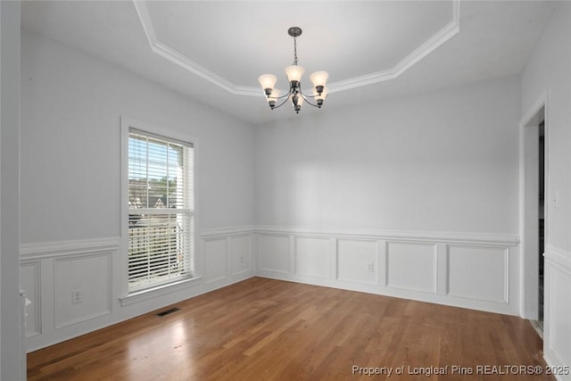 empty room featuring crown molding, a tray ceiling, a chandelier, and hardwood / wood-style flooring