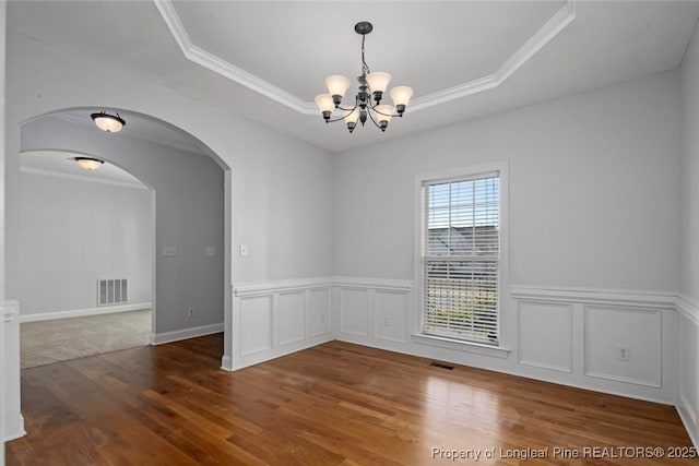 unfurnished room featuring an inviting chandelier, dark wood-type flooring, ornamental molding, and a raised ceiling