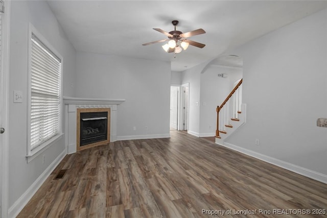 unfurnished living room featuring a tile fireplace, dark wood-type flooring, and ceiling fan