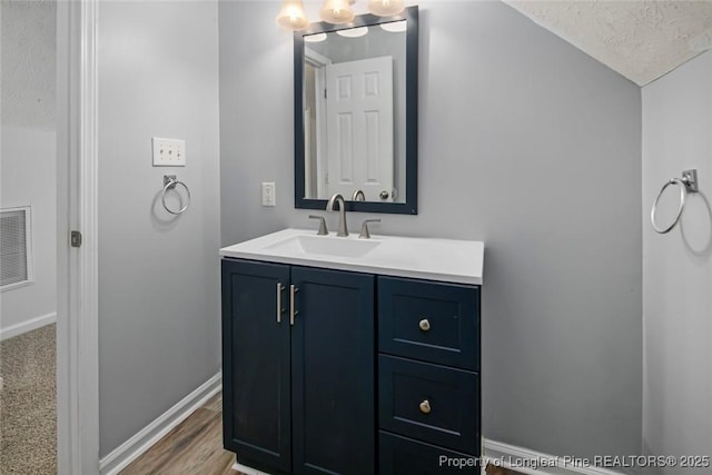 bathroom featuring vanity, vaulted ceiling, hardwood / wood-style floors, and a textured ceiling