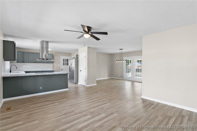 unfurnished living room featuring ceiling fan, sink, a textured ceiling, and light wood-type flooring