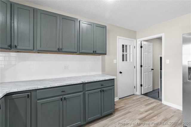 kitchen featuring gray cabinetry, a textured ceiling, light wood-type flooring, and decorative backsplash