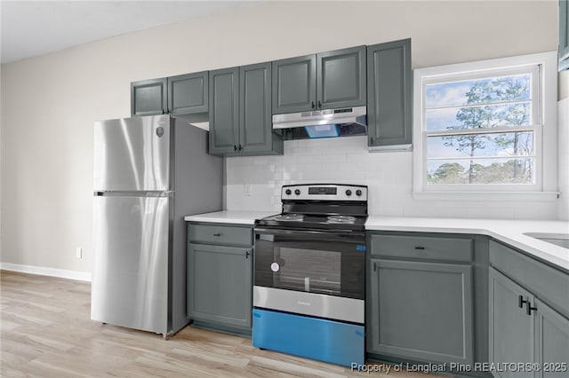 kitchen with tasteful backsplash, gray cabinets, light hardwood / wood-style flooring, and appliances with stainless steel finishes