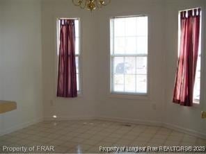 empty room featuring a chandelier, tile patterned flooring, and baseboards