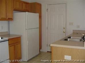 kitchen with stove, a sink, light countertops, freestanding refrigerator, and brown cabinetry