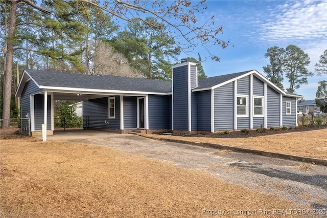 view of front of house with a carport, roof with shingles, driveway, and a chimney