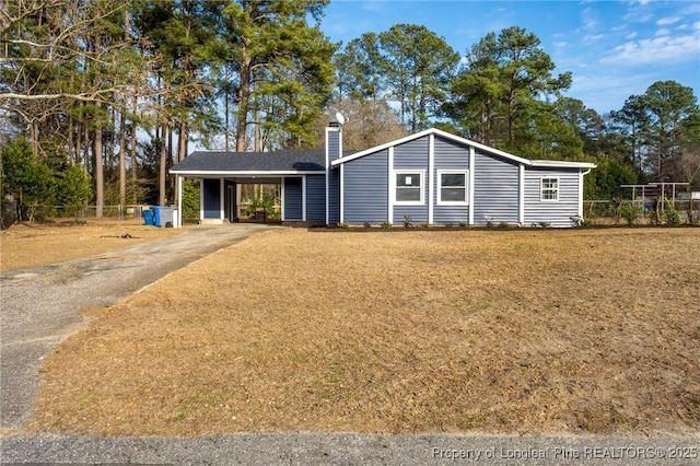 view of front of home with driveway, an attached carport, a chimney, and fence