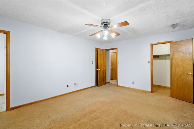 unfurnished bedroom with a walk in closet, light colored carpet, a textured ceiling, and baseboards