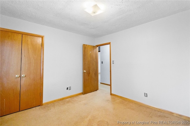 unfurnished bedroom with a textured ceiling, a closet, baseboards, and light colored carpet