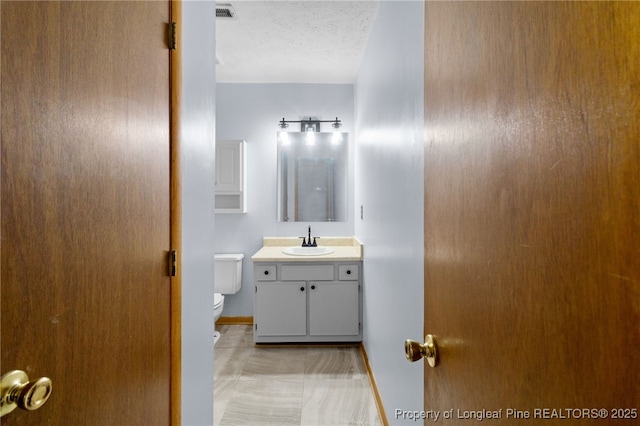 bathroom featuring visible vents, toilet, a textured ceiling, vanity, and baseboards