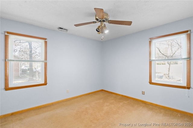 carpeted spare room with a ceiling fan, visible vents, a textured ceiling, and baseboards