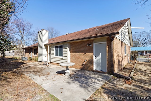 back of house with a patio area, a chimney, fence, and brick siding