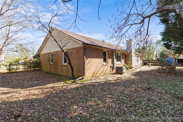 view of home's exterior featuring driveway, a chimney, fence, central AC, and brick siding