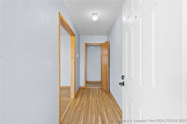 hall with light wood-style floors, a textured ceiling, and baseboards