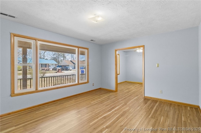 empty room featuring baseboards, visible vents, a textured ceiling, and light wood finished floors