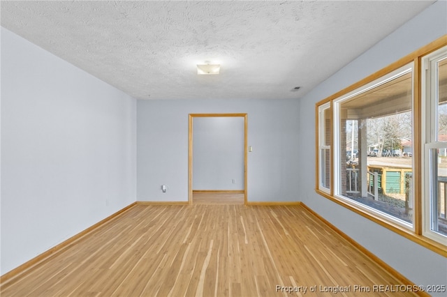 spare room with light wood-type flooring, a textured ceiling, and baseboards