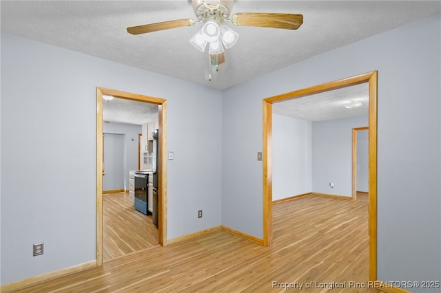 empty room with a textured ceiling, baseboards, and light wood-style floors