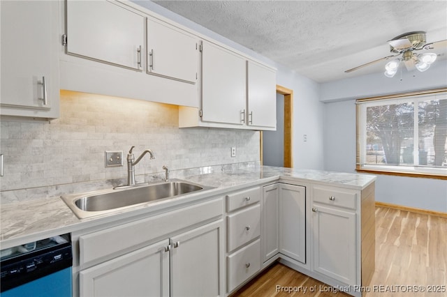 kitchen featuring light countertops, white cabinetry, a sink, dishwasher, and a peninsula