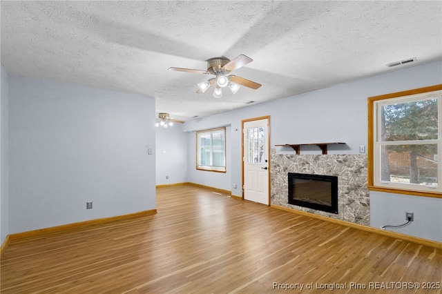 unfurnished living room with visible vents, a ceiling fan, a glass covered fireplace, wood finished floors, and baseboards