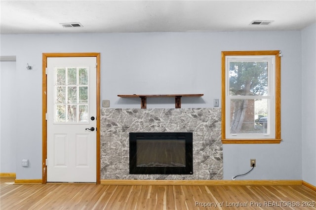 interior space with a stone fireplace, wood finished floors, visible vents, and baseboards