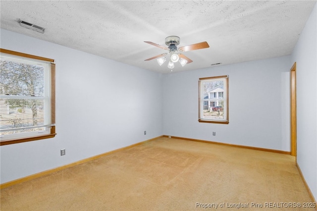 empty room with light carpet, ceiling fan, visible vents, and baseboards