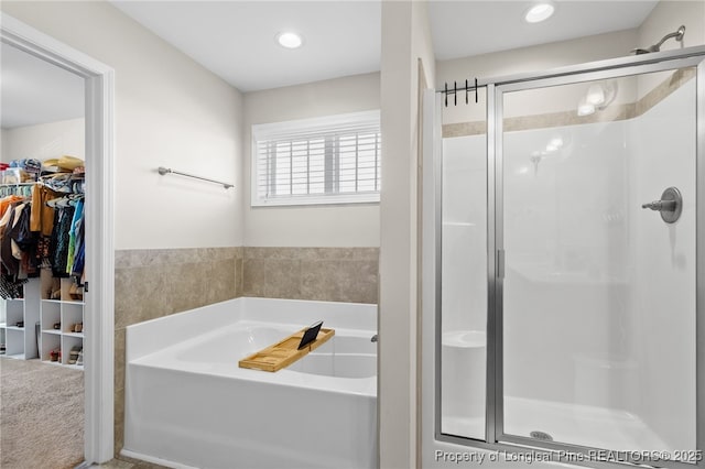 bathroom with a walk in closet, a garden tub, a shower stall, and recessed lighting