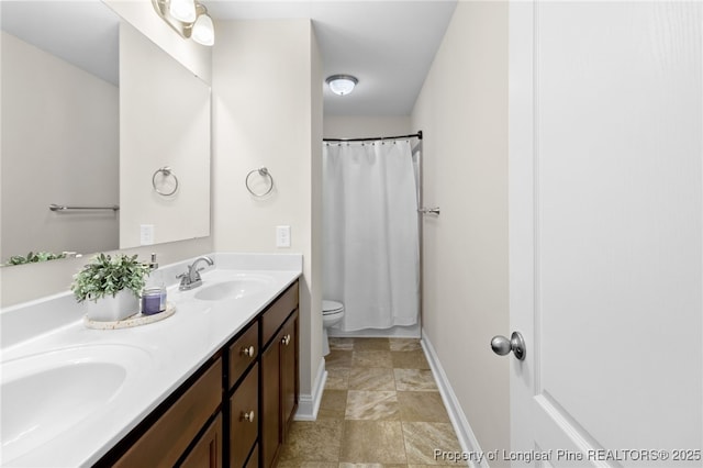 full bath featuring baseboards, a sink, toilet, and double vanity