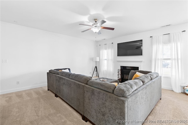 living area with a healthy amount of sunlight, ceiling fan, light carpet, and a glass covered fireplace