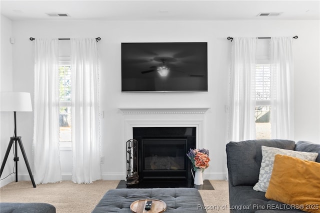 living area with a fireplace with flush hearth, a wealth of natural light, visible vents, and light colored carpet