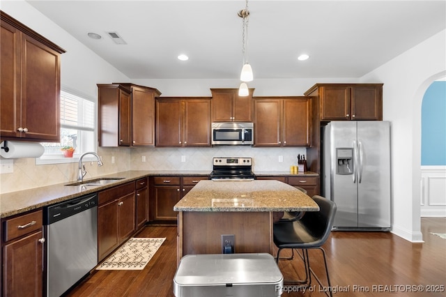 kitchen with stainless steel appliances, pendant lighting, a kitchen island, and light stone countertops