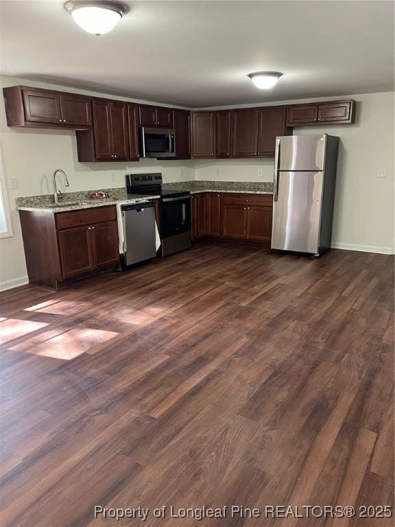 kitchen featuring baseboards, a sink, stainless steel appliances, dark wood-type flooring, and dark brown cabinetry