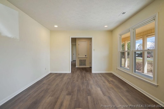 empty room featuring dark wood finished floors, visible vents, baseboards, and a textured ceiling