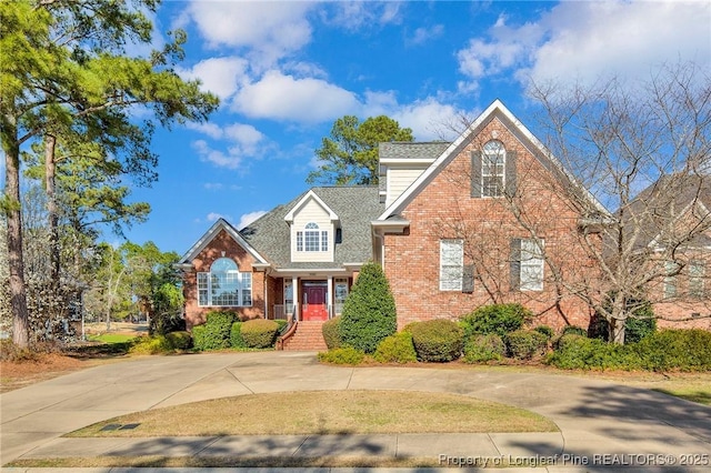 traditional home with brick siding, roof with shingles, and curved driveway