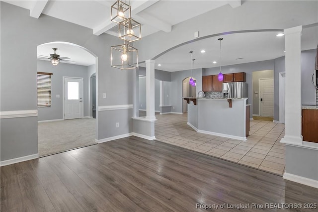 kitchen with a ceiling fan, open floor plan, stainless steel fridge, arched walkways, and light wood finished floors