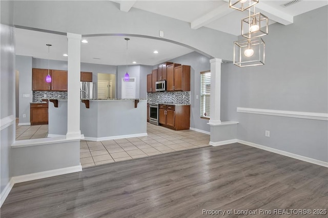 kitchen with backsplash, appliances with stainless steel finishes, light wood-style flooring, and ornate columns